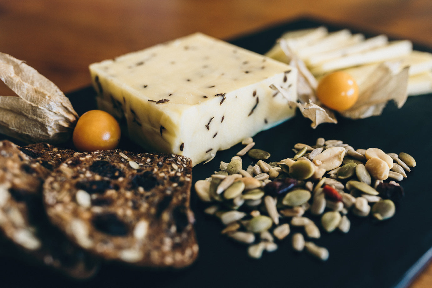 Caraway Jill cheese is served on a slate with seeded crackers and gooseberries. The cheese is flecked with whole caraway seeds.