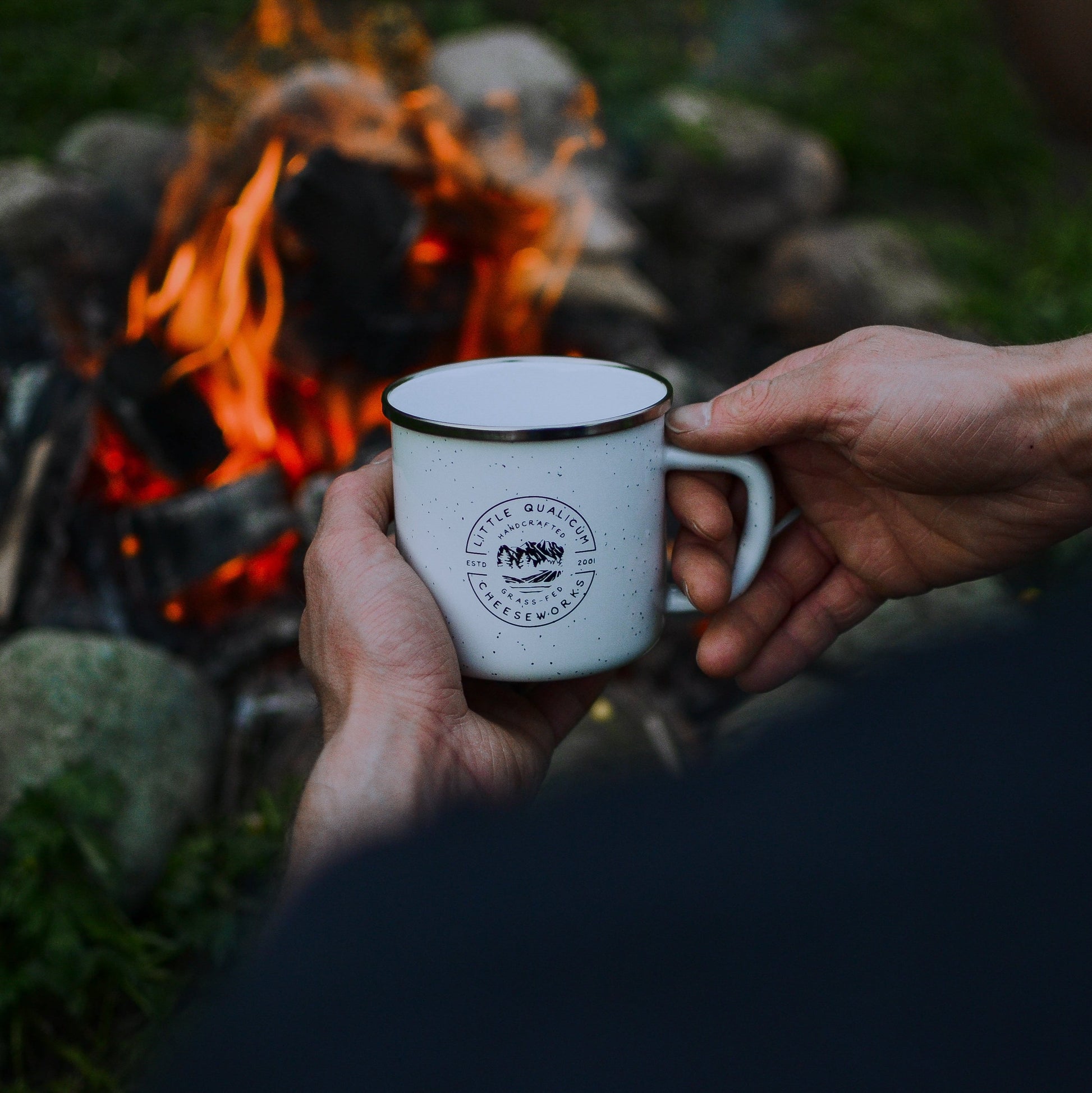 LQC logo mug held by person with campfire in background