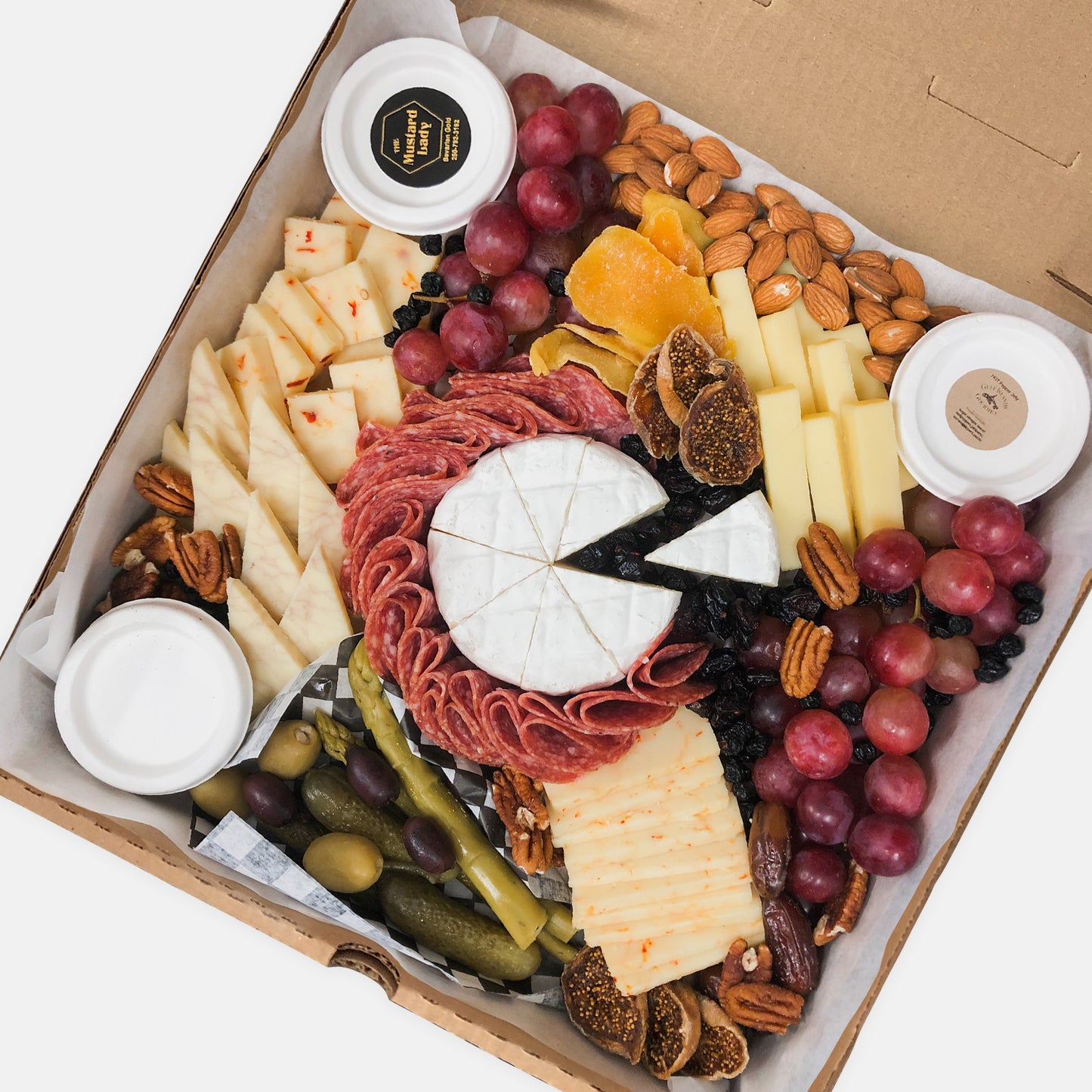 Large grazer box with cheese, nuts, meats, fruit, figs, pickled vegetables, olives, jelly and mustard in a pizza box