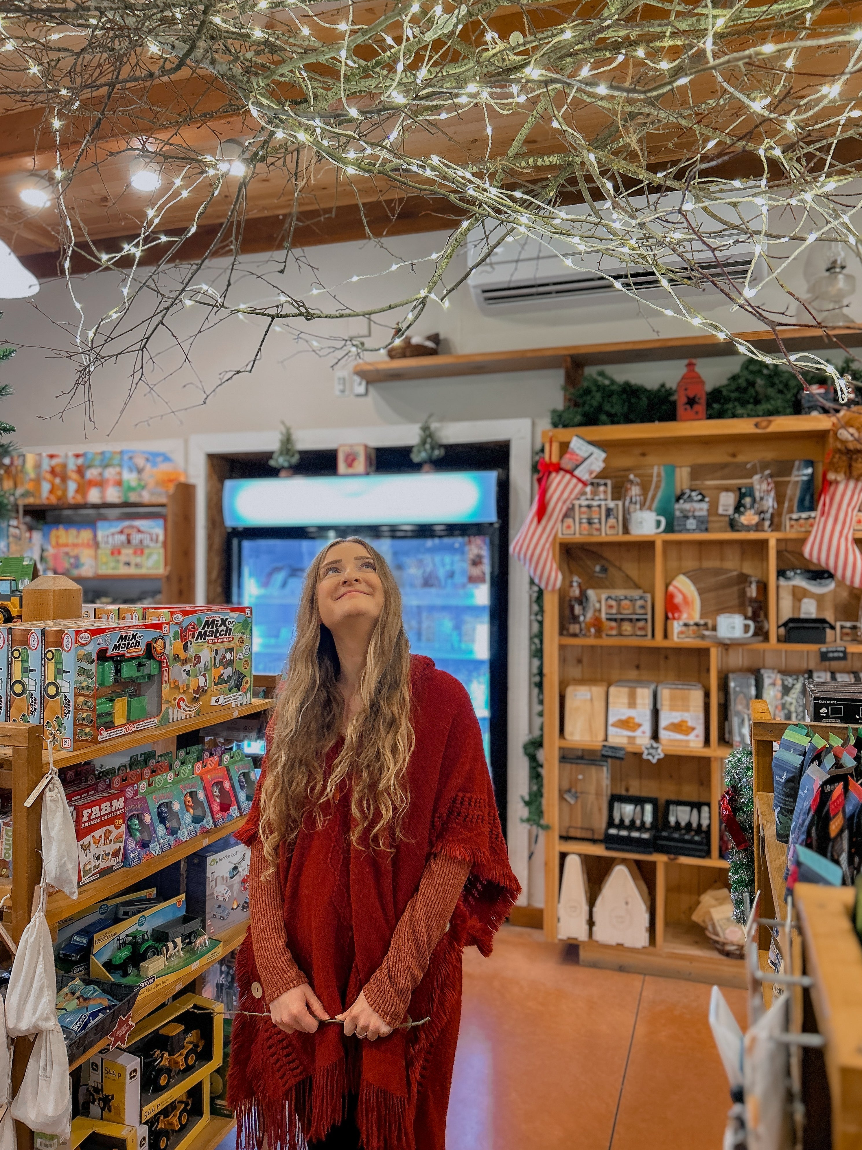 Woman in a red sweater standing in a store with shelves, products and decorations.