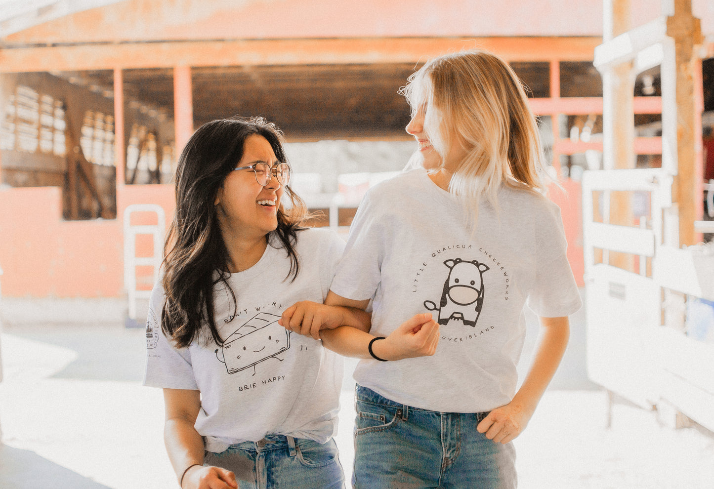 Two people wearing cheese and cow t-shirts in a barn setting.
