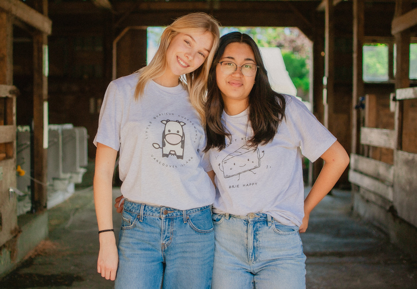 Two people wearing matching t-shirts with cow and cheese graphics in an barn setting.