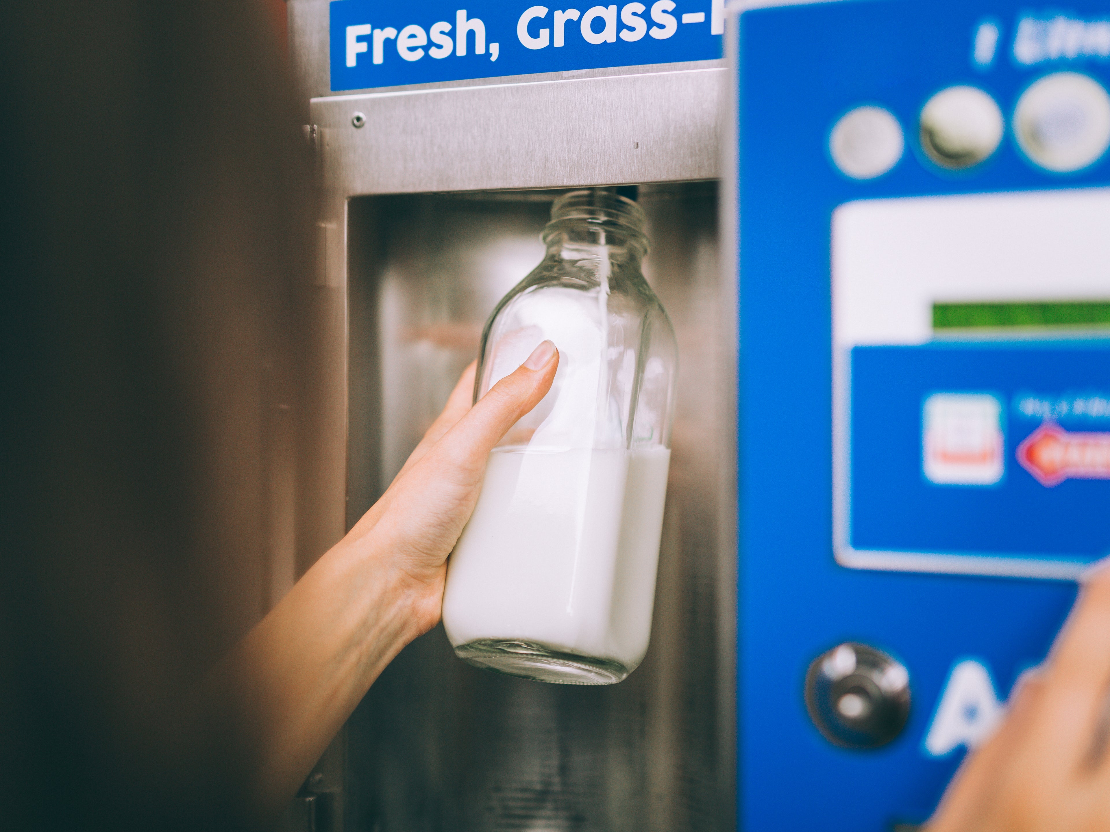 A person fills up their bottle at a self-serve milk on tap dispenser.