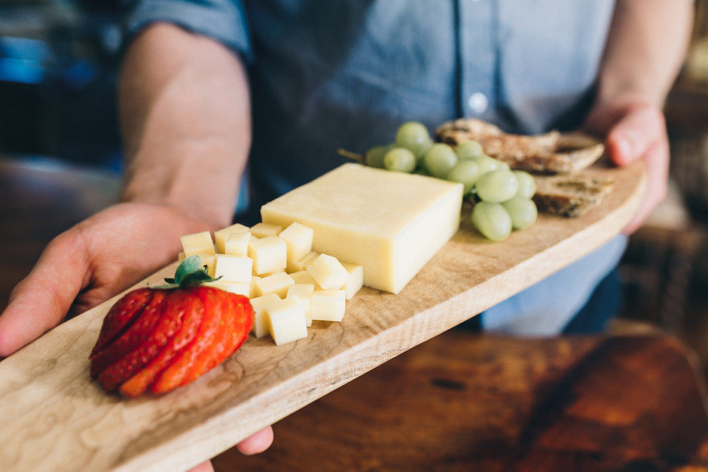 Monterey Jill cheese is served on a wooden board with sliced strawberry, grapes, and bread. The cheese is cut into cubes.