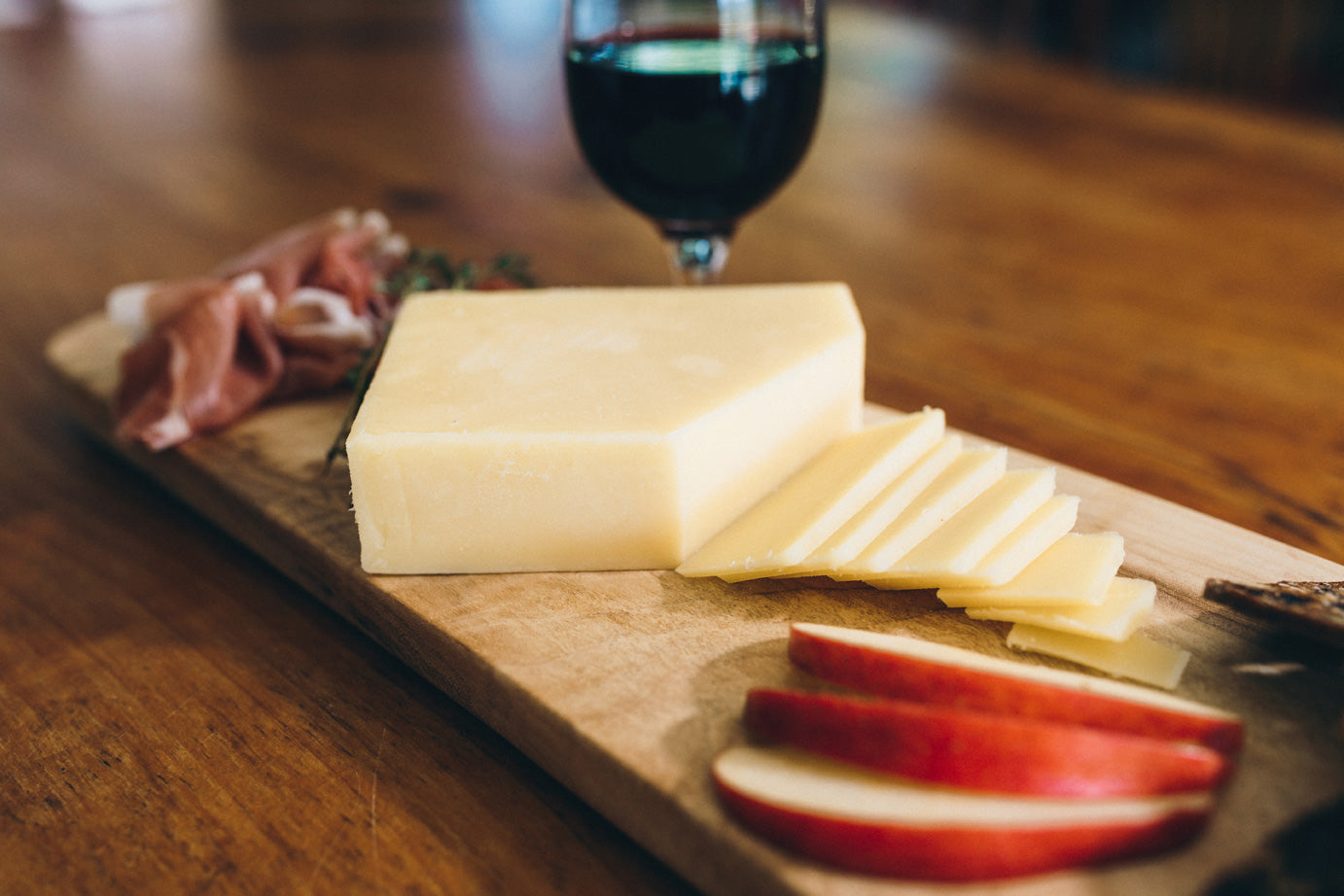 Mount Moriarty cheese is served on a wooden board with slices apples, sliced cured meats, and a glass of red wine.