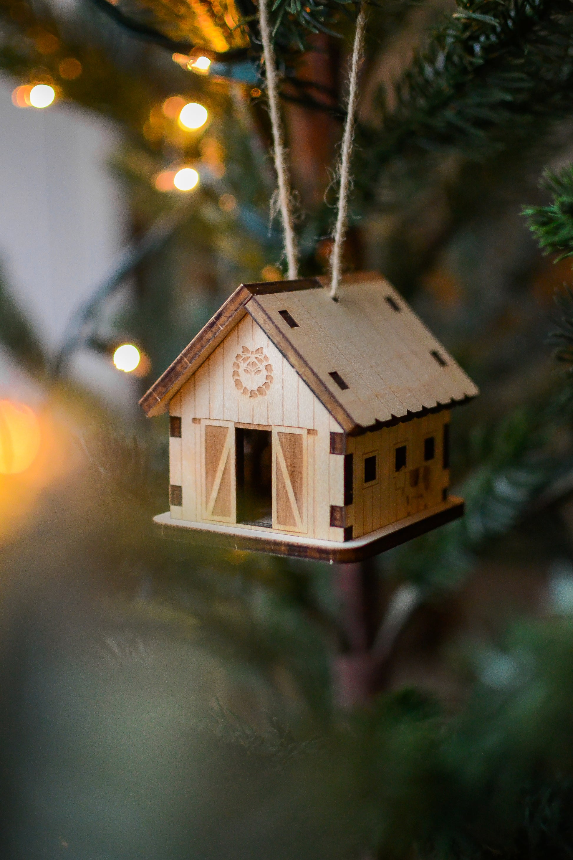 The assembled barn ornament hangs from the branch of an evergreen tree.