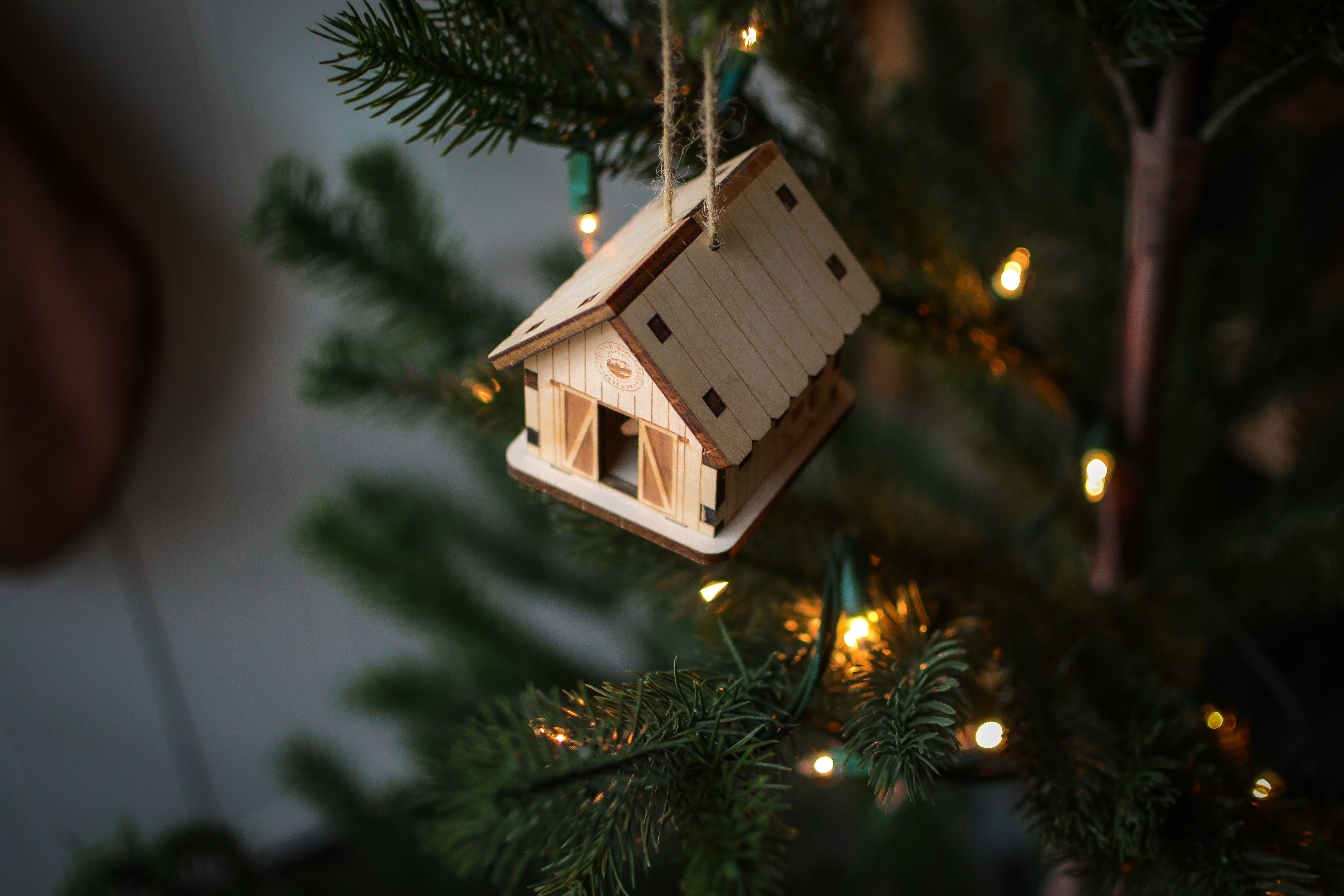 The assembled barn ornament hangs from the branch of an evergreen tree.