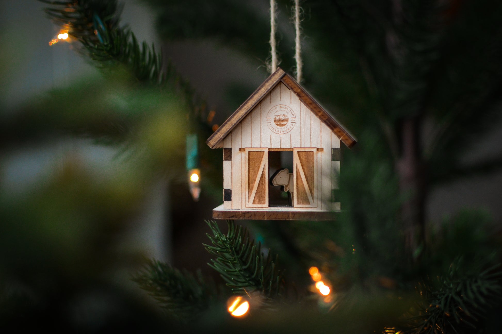 The assembled barn ornament hangs from the branch of an evergreen tree.