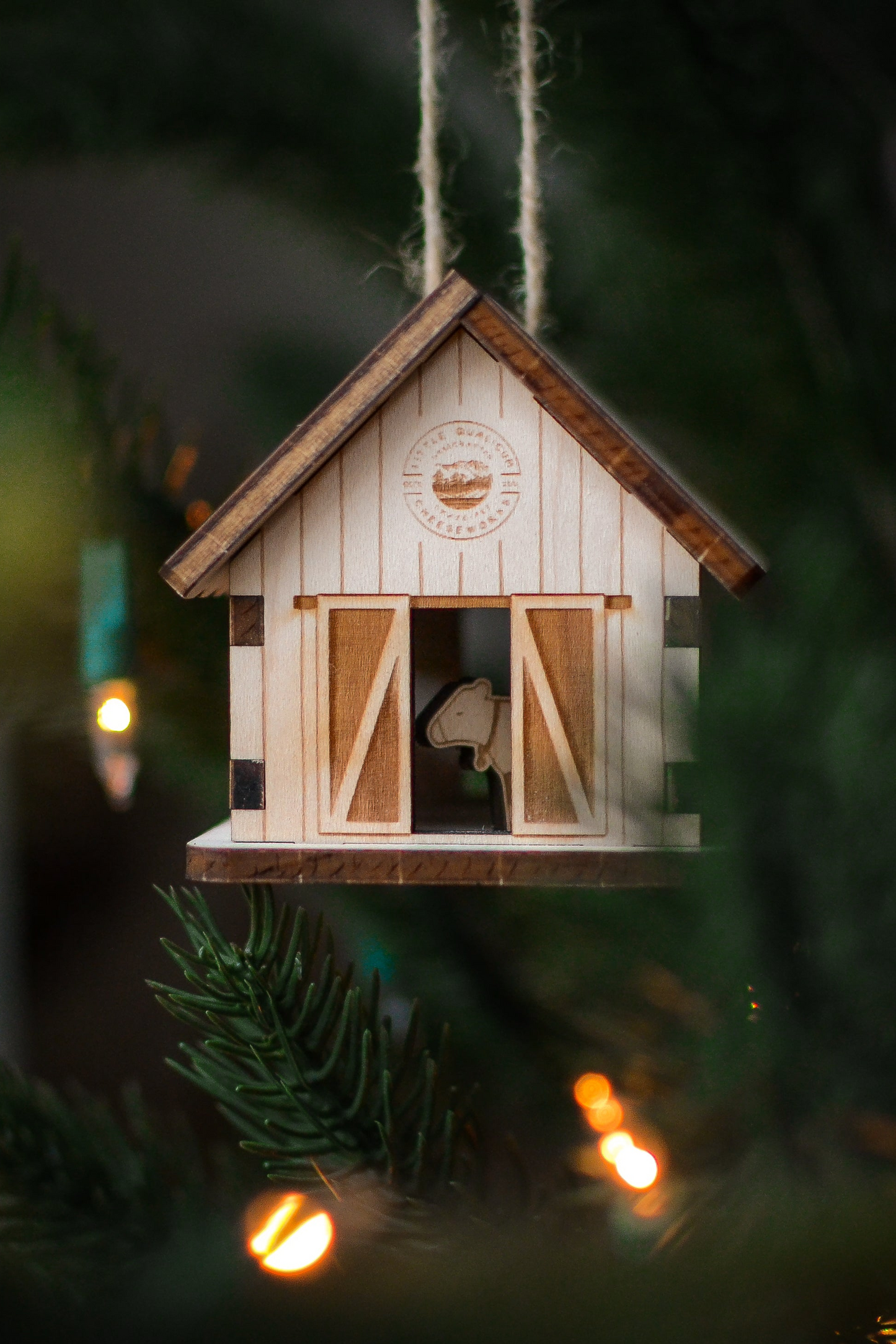 Wooden barn ornament hanging on tree with a cow peeking out of the barn 