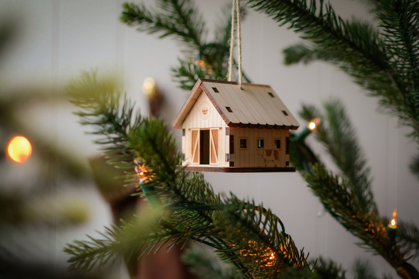 The assembled barn ornament hangs from the branch of an evergreen tree.