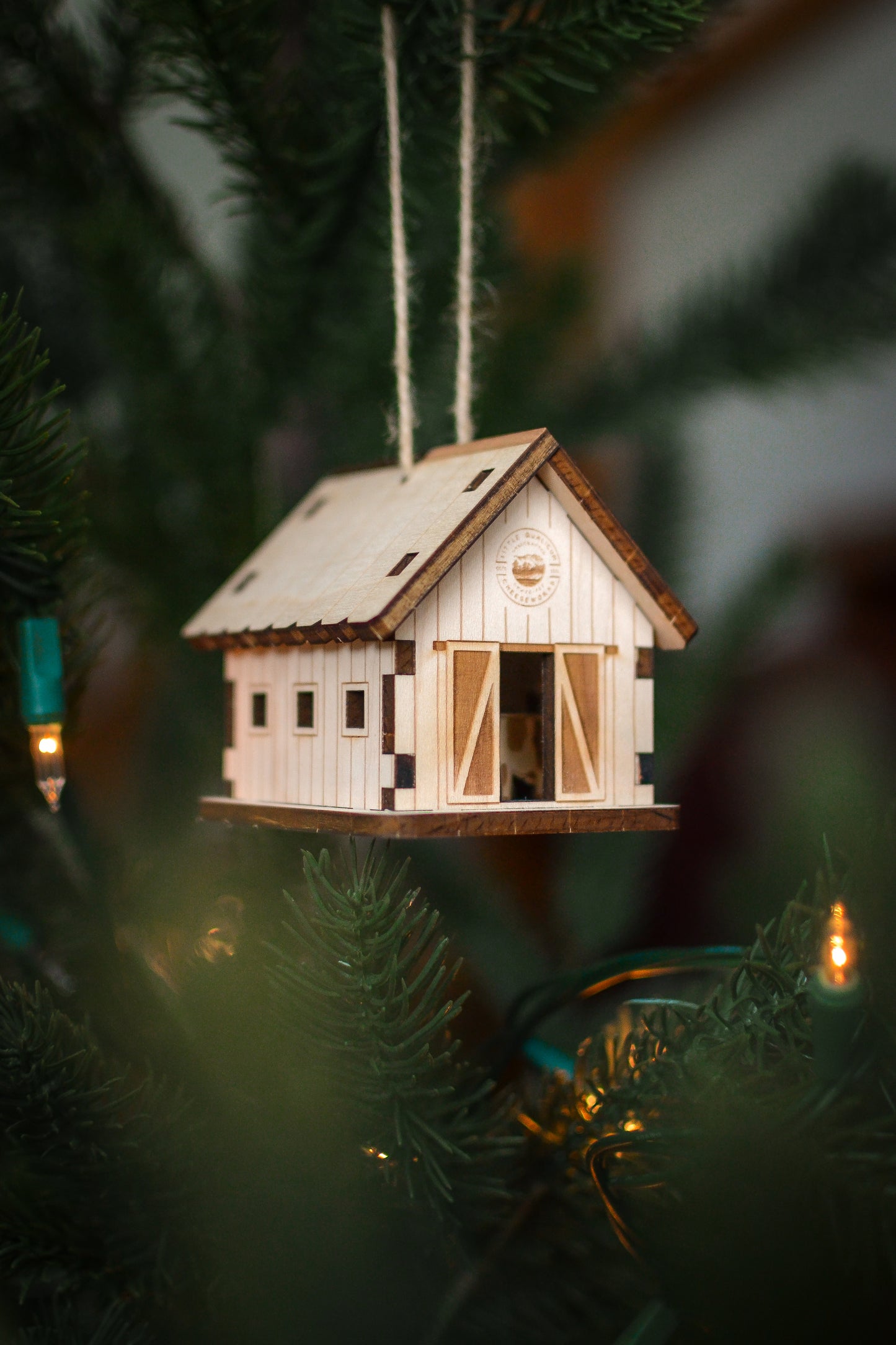 The assembled barn ornament hangs from the branch of an evergreen tree.