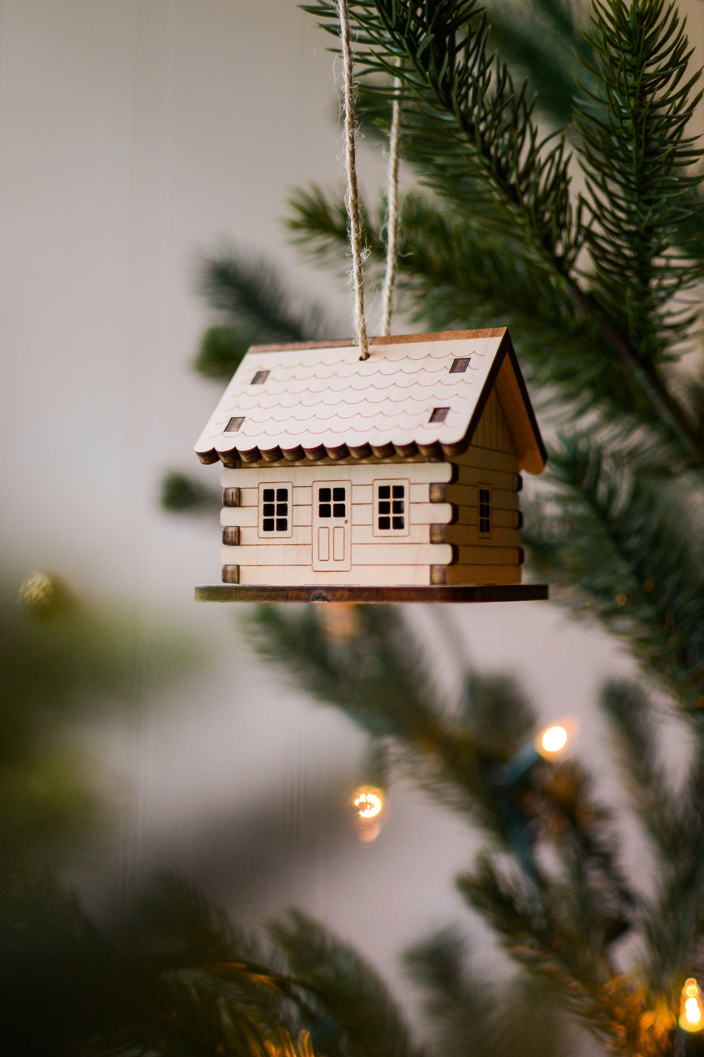 The assembled cabin hangs from an evergreen tree branch. Details include a scalloped roof, overlapping log corners, engraved horizontal log siding, and cut-out windows and doors.