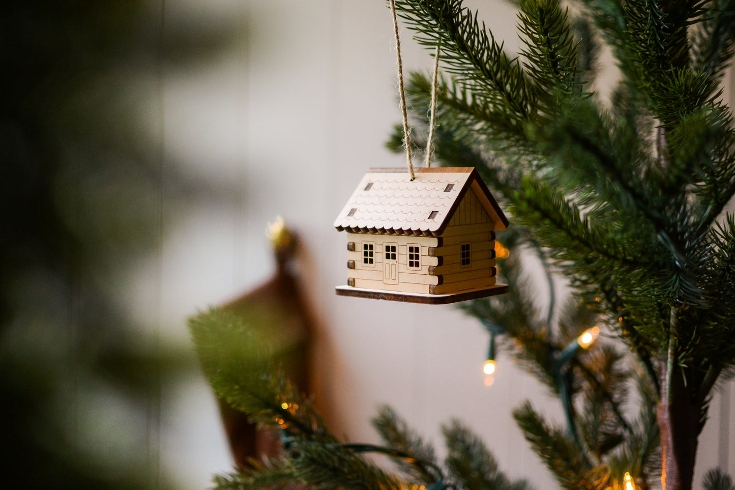 The assembled cabin hangs from an evergreen tree branch. Details include a scalloped roof, overlapping log corners, engraved horizontal log siding, and cut-out windows and doors.