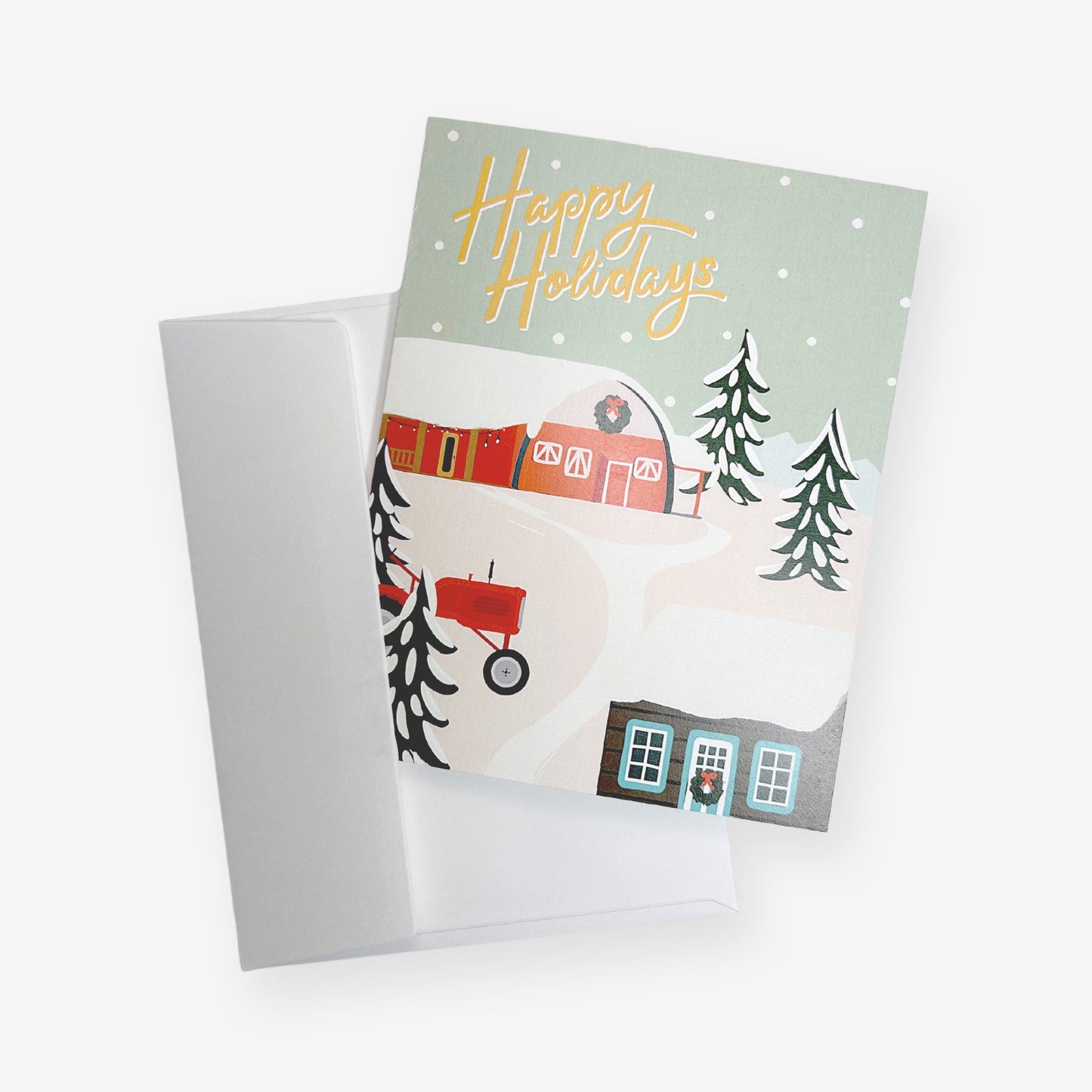 This Christmas card features a stylized illustration of a recognizable Little Qualicum Cheeseworks barn with the historic log cabin in the foreground. Both buildings are covered in snow and adorned with Christmas wreaths, garlands, and bows. A red tractor peeks out through a stand of snowy evergreen trees and mountains are in the far background of the snowy landscape. In the sky amidst falling snowflakes, "Happy Holidays" is written in a playful script. The card comes with a white envelope.