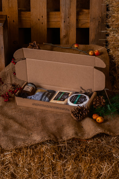 Open cardboard box with brie, qualicum spice, pepper and sea salt crackers, and gulf islands jelly on a rustic wooden and hay background