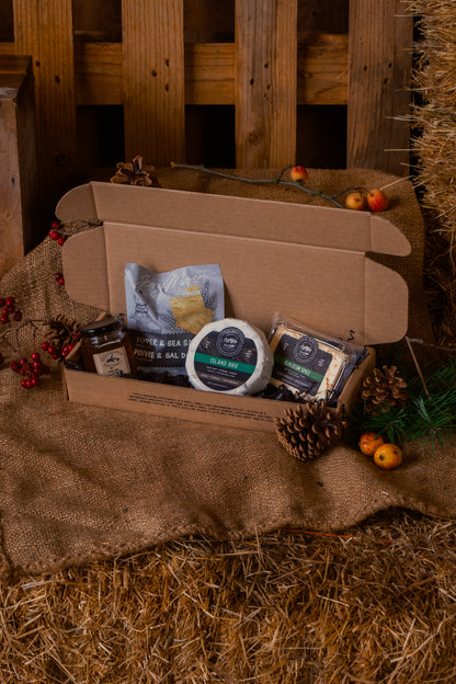 Open cardboard box with brie, qualicum spice, pepper & sea salt crackers and gulf islands jelly products on a rustic wooden and hay background
