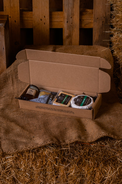 Open cardboard box with brie, qualicum spice, pepper and sea salt crackers and gulf islands jelly on a rustic wooden and hay background