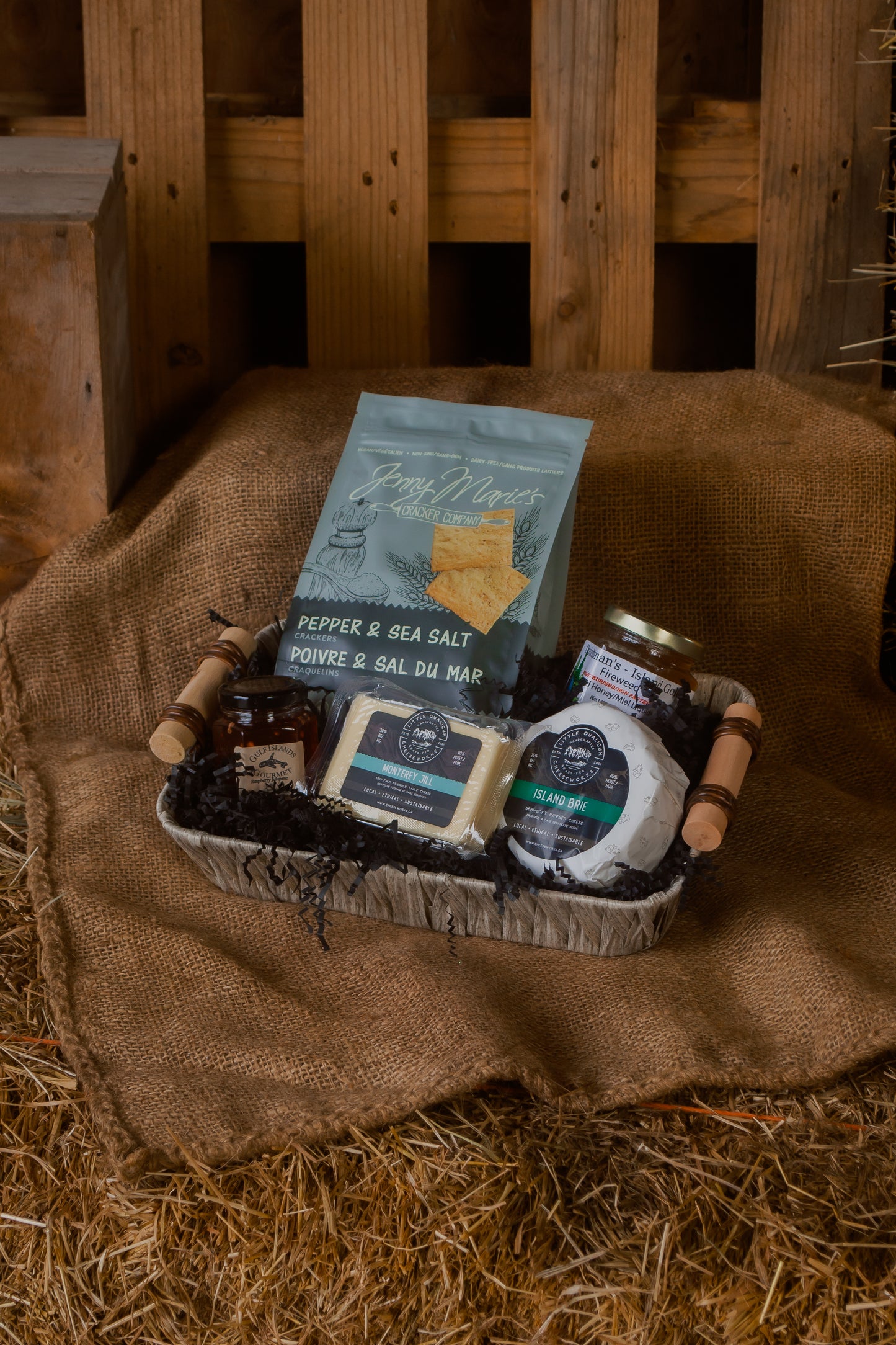 Assorted local Vancouver Island food products on a burlap cloth with a rustic wooden background, displayed as a gift basket