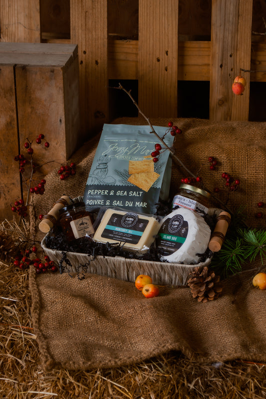 Gift basket with various items including crackers, honey, preserves, and cheese, set against a rustic wooden background.