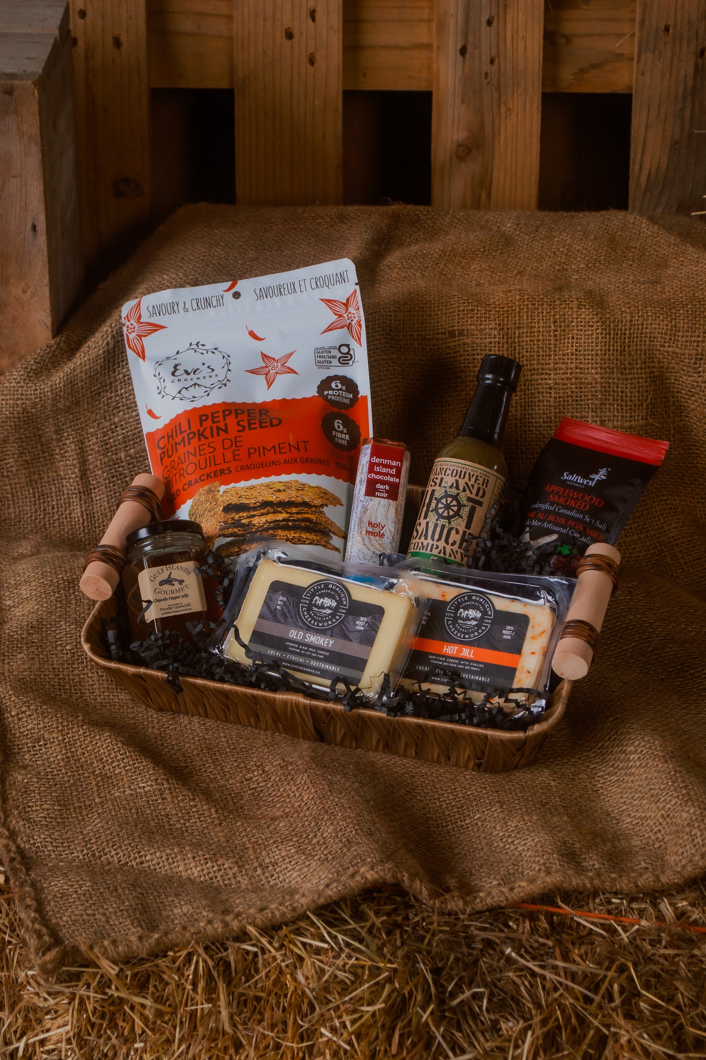 Assorted BC local food items in a gift basket, against a rustic wooden background.