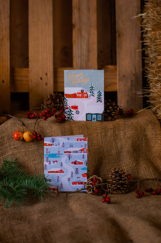 Two Christmas-themed cards on a rustic wooden background with pine cones and berries.