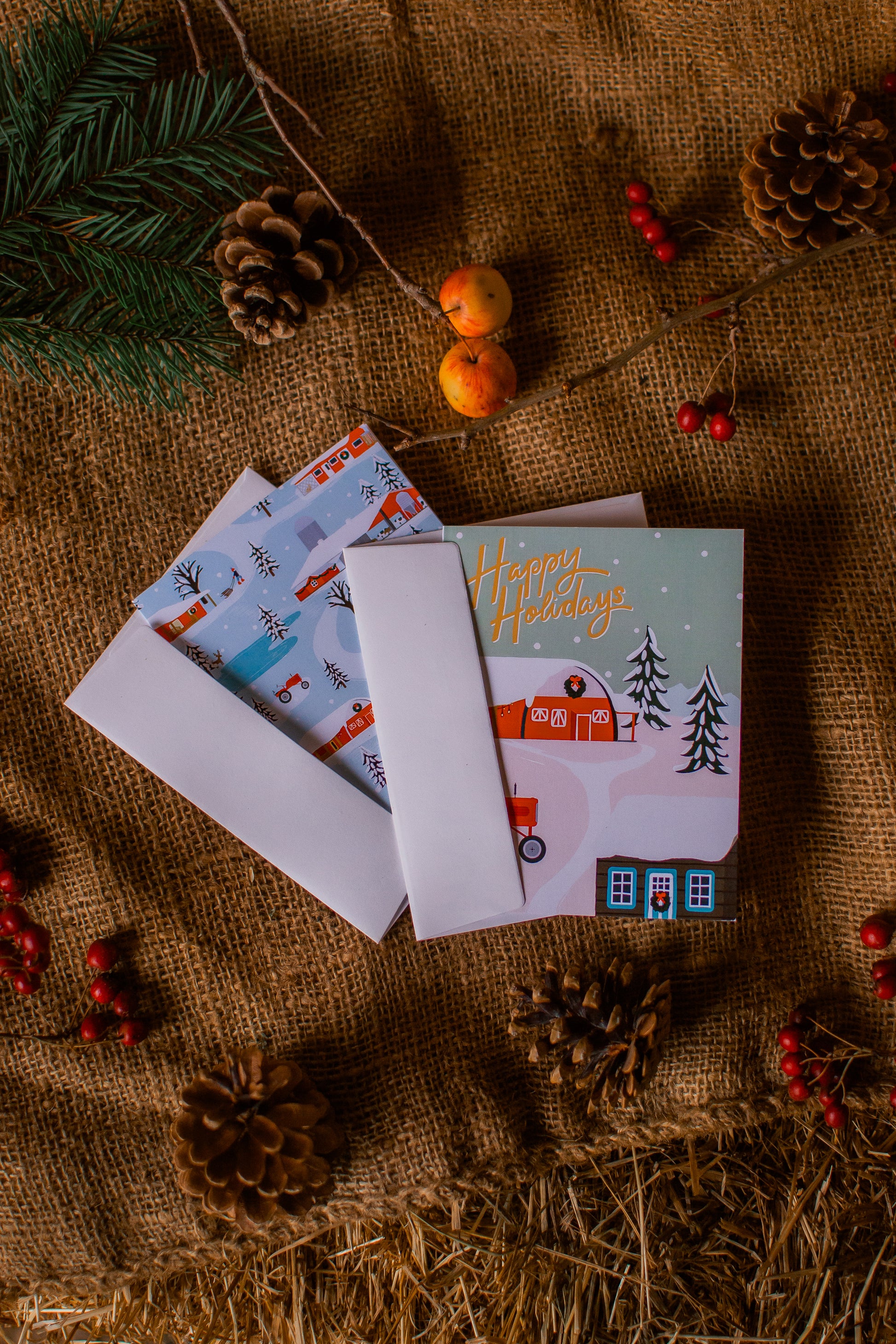 Set of Christmas cards with envelopes on a rustic background with pinecones and berries.