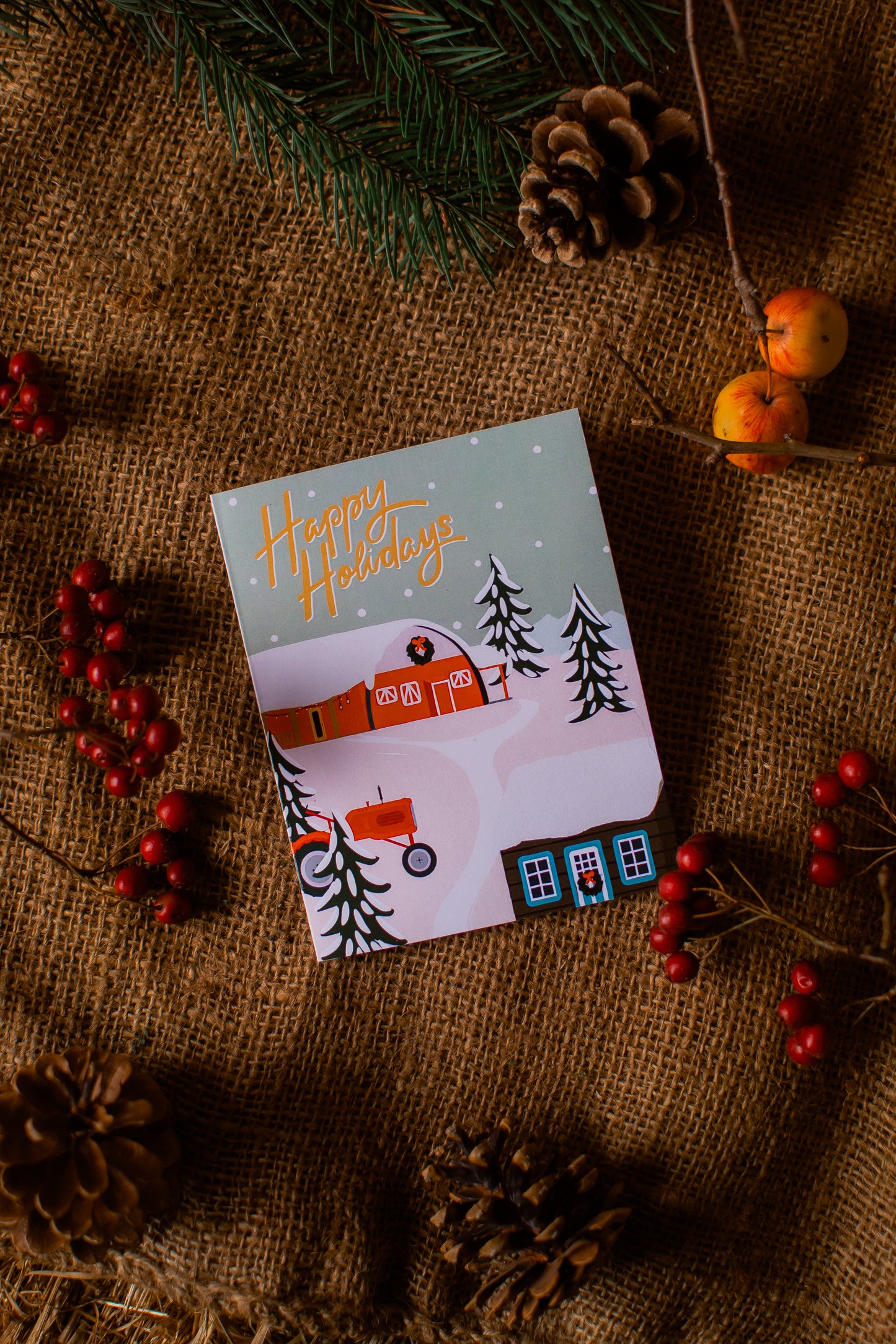 Holiday card with winter scene on a rustic background with pinecones and berries