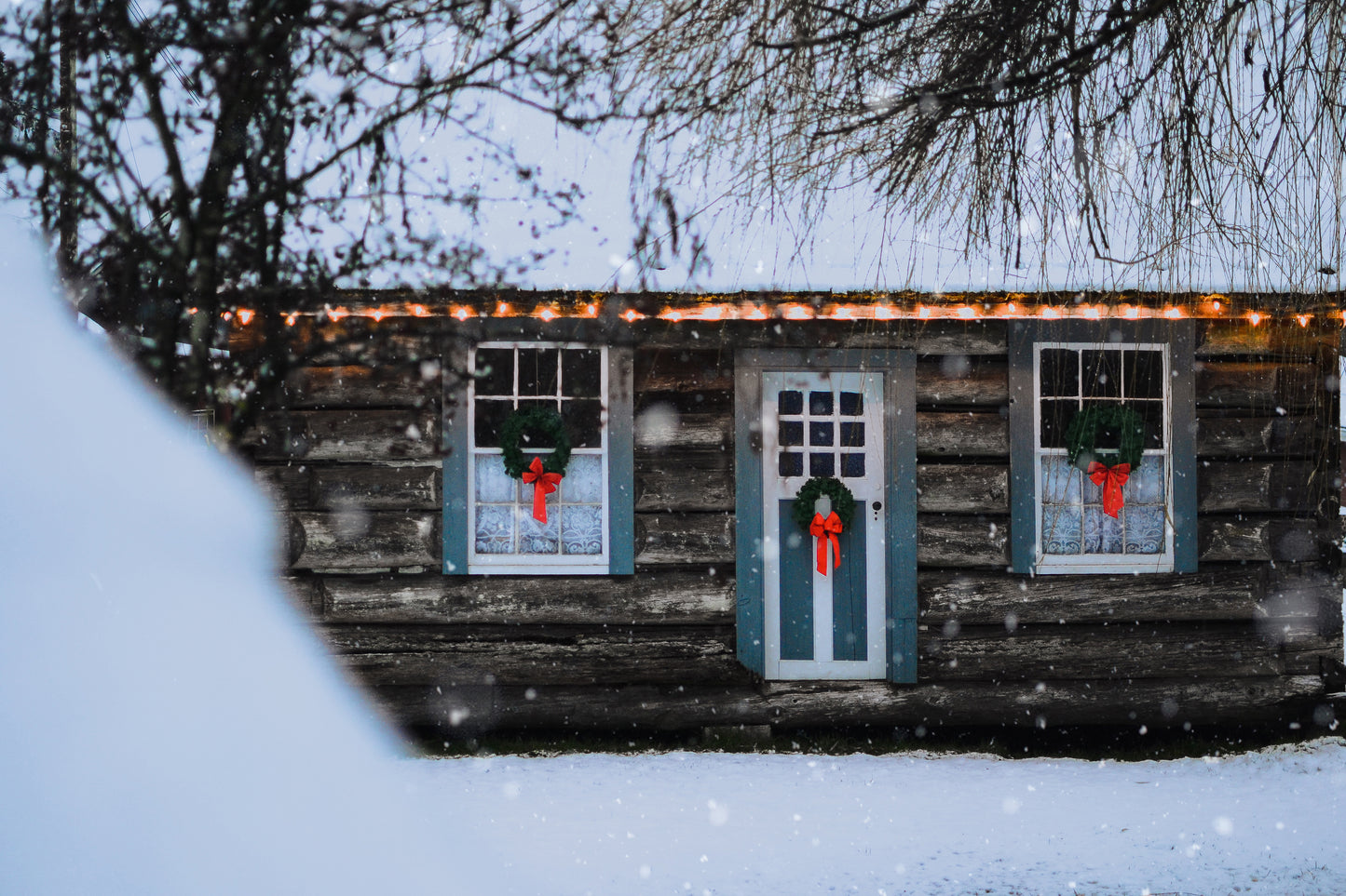 The heritage cabin at Little Qualicum Cheeseworks, adorned with wreaths on the windows and door and covered in a light dusting of snow.