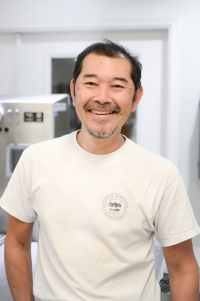 Employee wearing white LQC T shirt standing in front of metal machinery and white door 