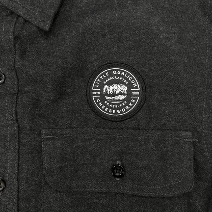 Dark gray shirt with a circular patch on the chest featuring Little Qualicum Cheeseworks' logo (a circular patch withtext and a mountain graphic).