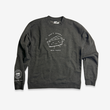 The artwork on the charcoal heather sweatshirt is printed in a contrasting white. The sweatshirt has long sleeves. At the lower end of the left sleeve near the cuff, the LQC logo is printed with "Vancouver Island" written below. On the front of the sweatshirt is an 8" line drawing of a personified wedge of Brie. The Brie dances with little arms in the air and smiles. The text  "Don't worry, Brie happy" is written around the illustration.