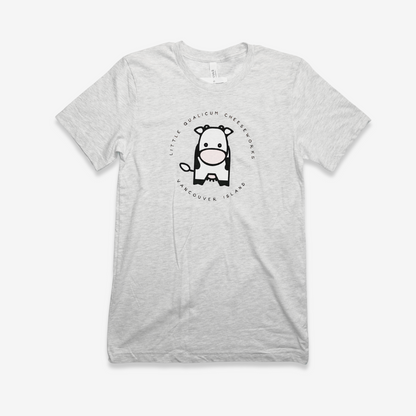 The front of the shirt shows a simplified cute 8" illustration of a Holstein dairy cow from the front. The text "Little Qualicum Cheeseworks Vancouver Island" is written in a circle around the cow.